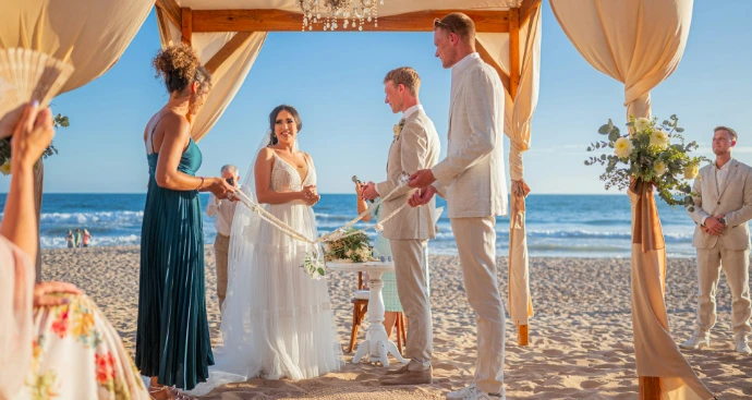 A wedding ceremony on a sunny beach with ocean backdrop.